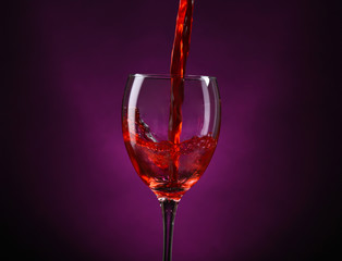 Wine pouring in glass on dark purple background