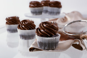Chocolate cupcakes with sieve on light glass background, close up