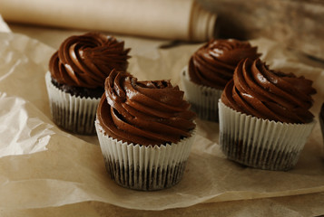 Chocolate cupcakes on baker paper over wooden background