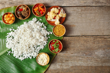 Boiled rice with vegetables and spices on banana leaf over wooden background
