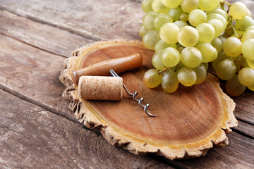 Wine cork and tailspin with bunch of grapes on wooden background