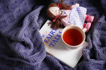 Rag doll with fairy tales book and cup of tea on bedspread. Childhood concept
