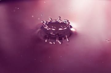 Macro photo of water drops falling into a pool of water, causing a splash and ripples.