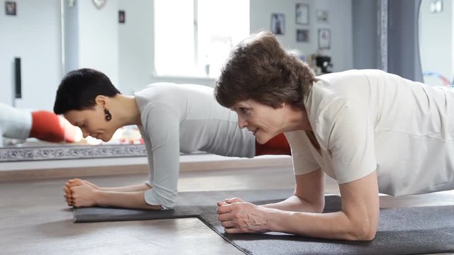 Young girl and senior woman doing plank exercise in yoga class