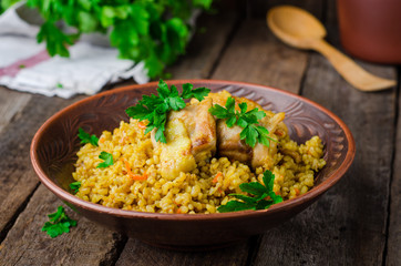 Chicken bulgur pilaf in clay bowl on wooden background. Selective focus