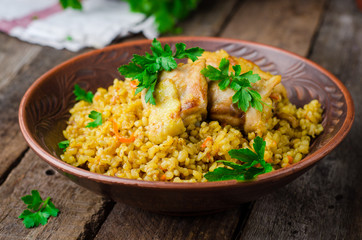 Chicken bulgur pilaf in clay bowl on wooden background. Selective focus