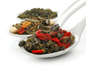 Different sorts of dry tea in ceramic spoons, isolated on white