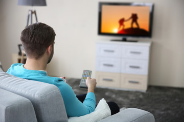 Young handsome man watching TV on a sofa at home