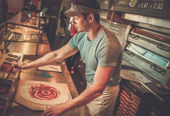 Handsome pizzaiolo making pizza at kitchen in pizzeria.