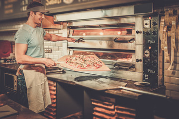 Handsome pizzaiolo making pizza at kitchen in pizzeria.