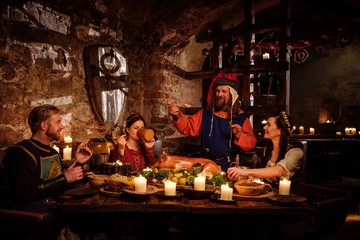 Medieval people eat and drink in ancient castle kitchen interior.