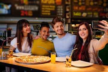 Cheerful multiracial friends taking selfie in pizzeria.