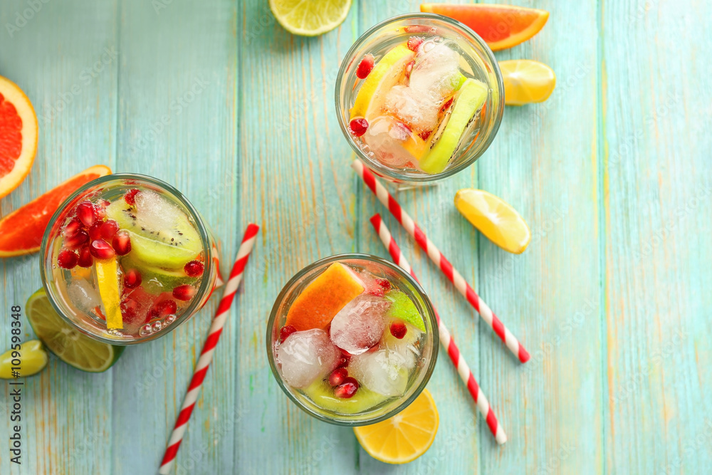 Wall mural Refreshing cocktails with ice, mint, pomegranate seeds and slices of fruits on blue wooden background