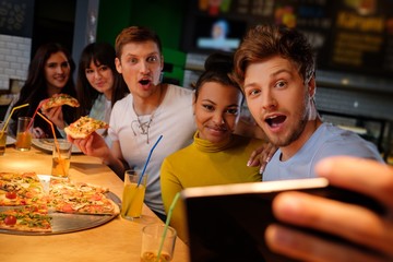 Cheerful multiracial friends having fun eating in pizzeria.