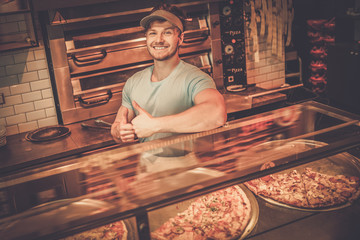Handsome pizzaiolo standing at kitchen in pizzeria.