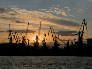 Fototapeta premium Silhouette of port cranes on sunset sky background
