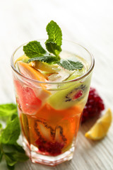 Refreshing cocktail with ice, mint, pomegranate seeds and slices of fruits on light wooden background