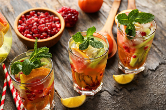 Refreshing cocktails with ice, mint, pomegranate seeds and slices of fruits on rustic wooden background