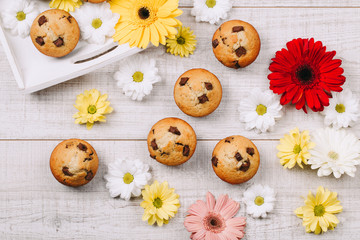 Homemade chocolate chip muffins on a white wooden table decorated with flowers. Old film look.