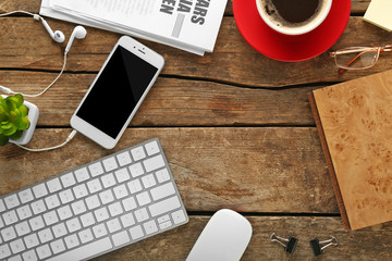 Workplace with mobile phone, peripheral devices and newspaper on wooden table