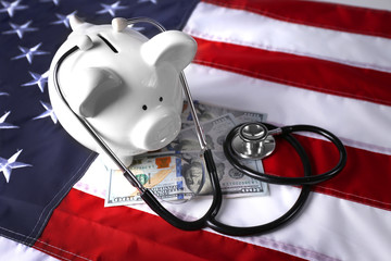 Stethoscope with dollar banknotes and piggy bank on background of USA flag