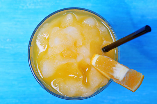 Glass of orange juice with crushed ice on blue wooden table