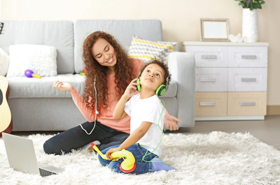 Young woman in headphones listens little boy playing on toy saxophone.