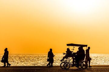 Fototapeta na wymiar Silhouettes of people enjoying a walk by the seaside of the town