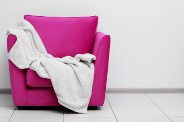 Pink armchair with blanket on light wall background
