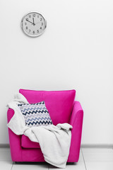 Pink armchair with blanket and pillow on light wall background
