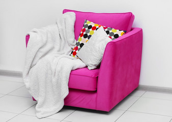 Pink armchair with blanket and pillows on light wall background
