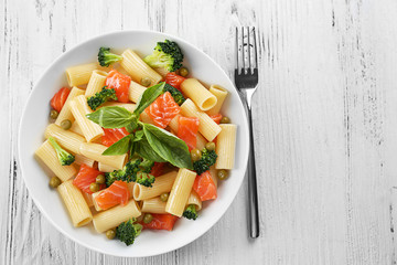 Plate of pasta with salmon and broccoli on wooden table, top view