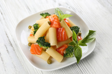 Plate of pasta with salmon and broccoli on table closeup