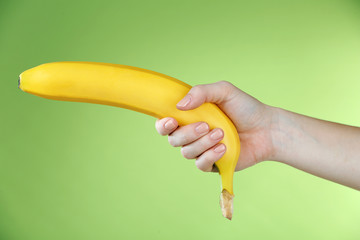 Female hand holding banana on green background
