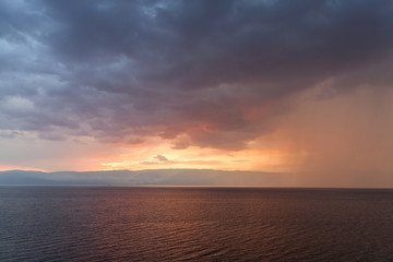 Rain storms are happening at sea in sunset time