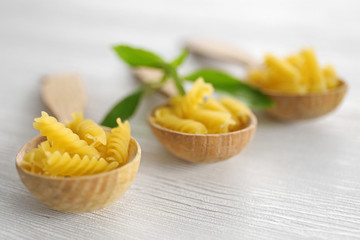 Fresh uncooked pasta in wooden spoons on table closeup