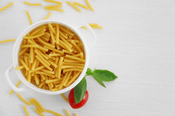 Fresh uncooked pasta in bowl on wooden table, top view