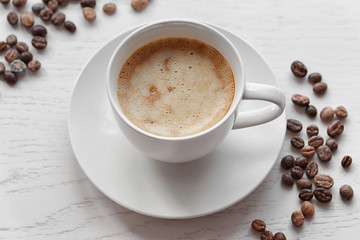 Cup of coffee and coffee beans on light wooden background