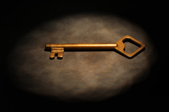 Old key on dark surface with beam of light