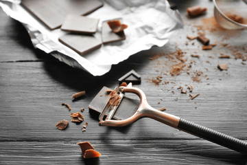 Piece of chocolate with peeler on black wooden background