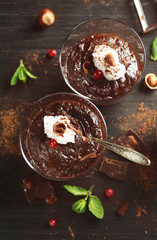 Glass cups of chocolate dessert with cranberries, fresh mint and frothed milk on black wooden table
