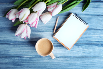 Bouquet of fresh tulips with cup of coffee and notebook on blue wooden background
