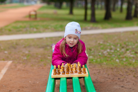 Little Girl playing chess outdoors on a park bench