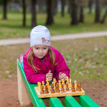 Little Girl playing chess outdoors on a park bench