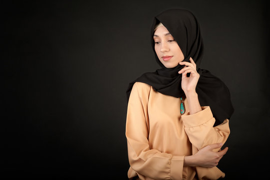 studio portrait of a young woman oriental appearance in the modern Muslim dress and covered her head against a dark background