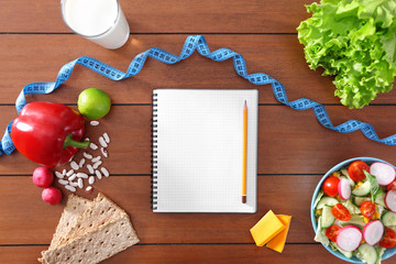 Healthy food, measuring tape and blank notebook on wooden table, top view