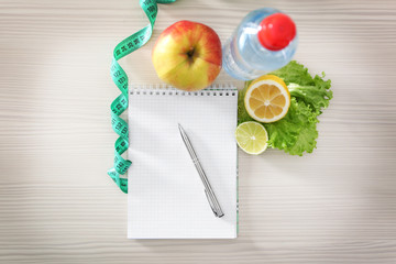 Blank notebook, measuring tape and healthy food on wooden table, top view