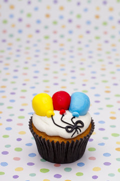 close-up image of cupcake decorated with colorful balloons.