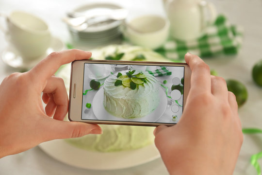 Female hands with smart phone making photo of a creamy lime cake closeup