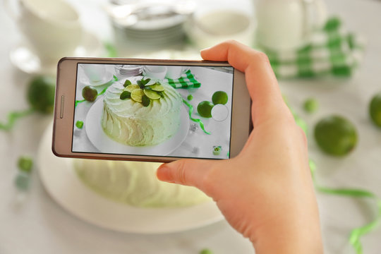 Female hand with smart phone making photo of a creamy lime cake closeup